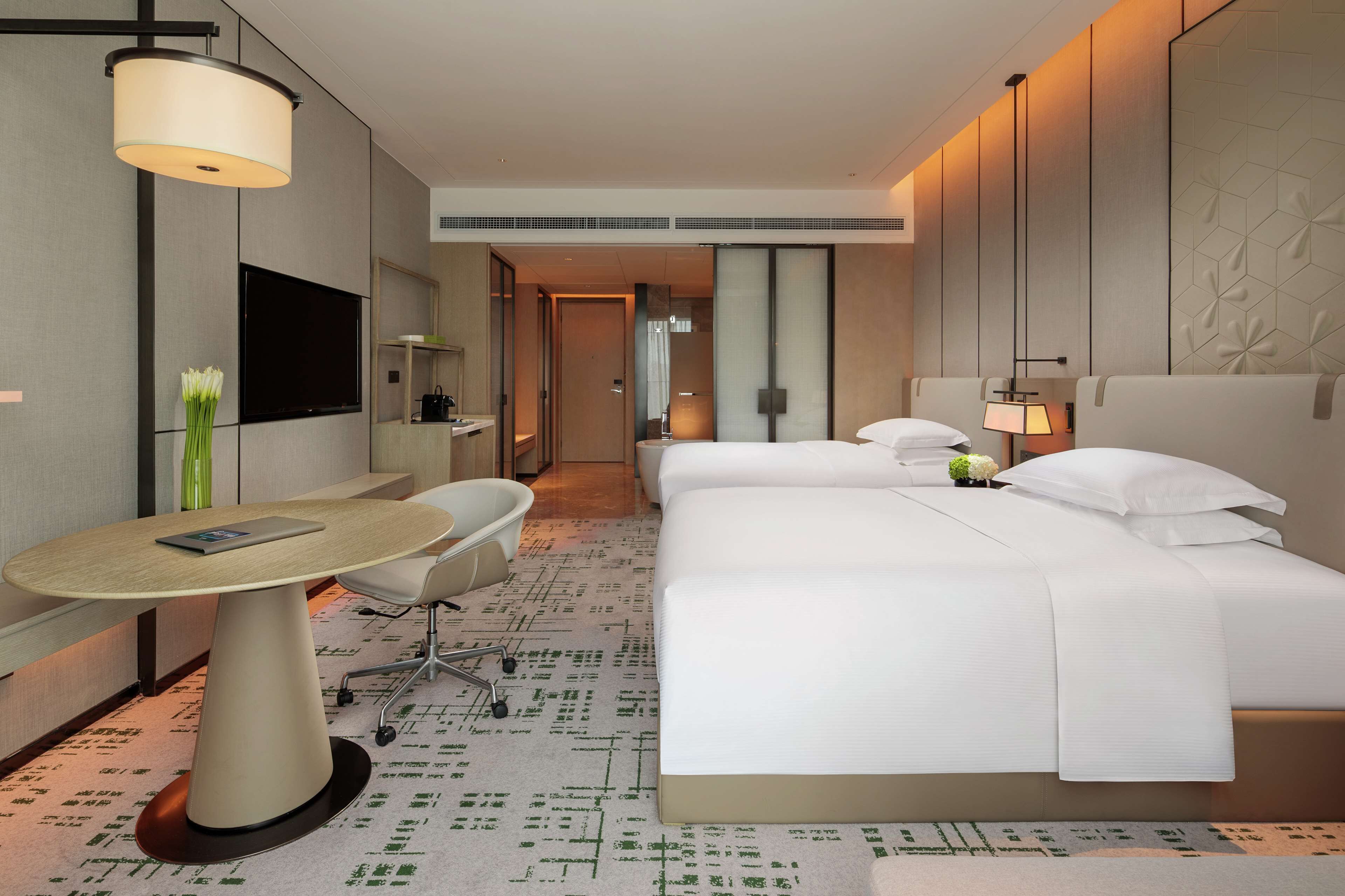 A hotel room with a bed, a desk, a chair, a TV, and a lamp.
