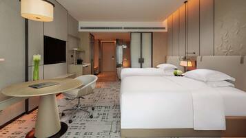 A hotel room with a bed, a desk, a chair, a TV, and a lamp.