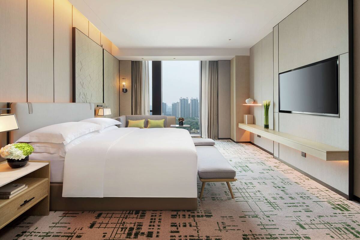 Una habitación de hotel moderna con una cama grande, un sofá, un televisor y vistas a la ciudad.