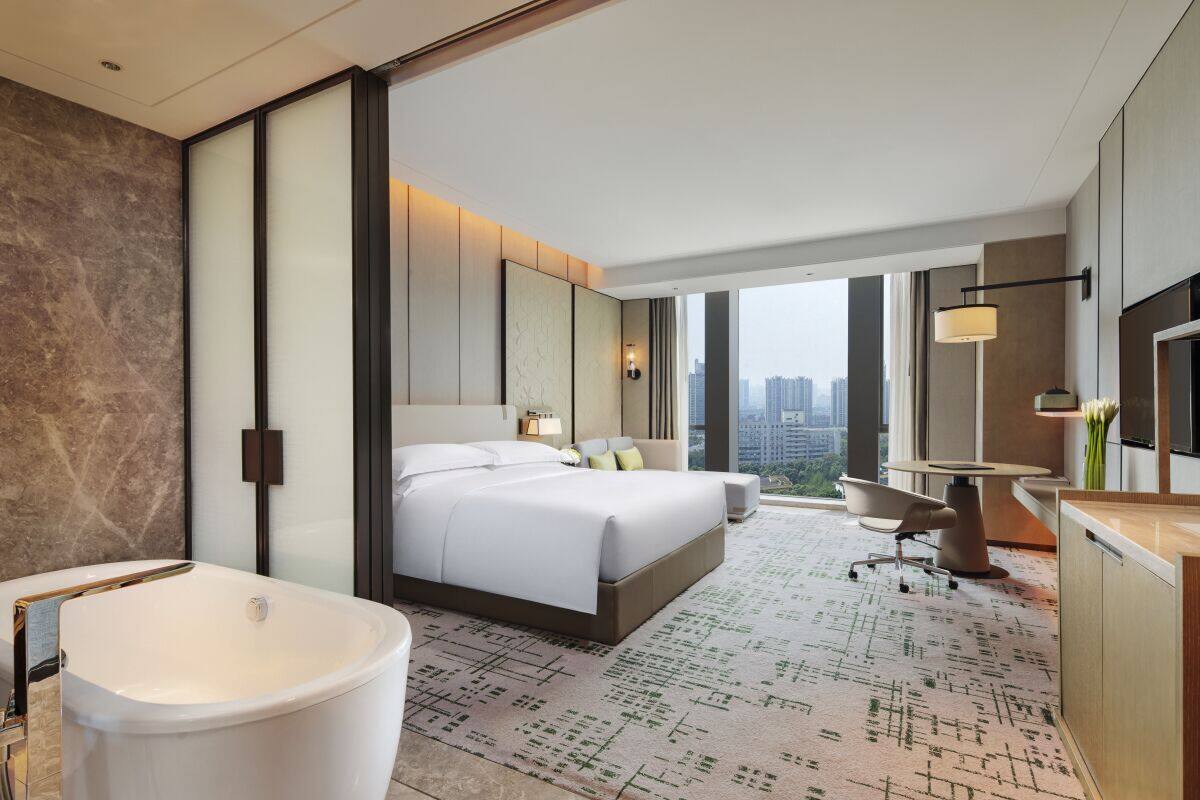 Una habitación de hotel moderna con una cama grande, una bañera, un escritorio y vistas de la ciudad.
