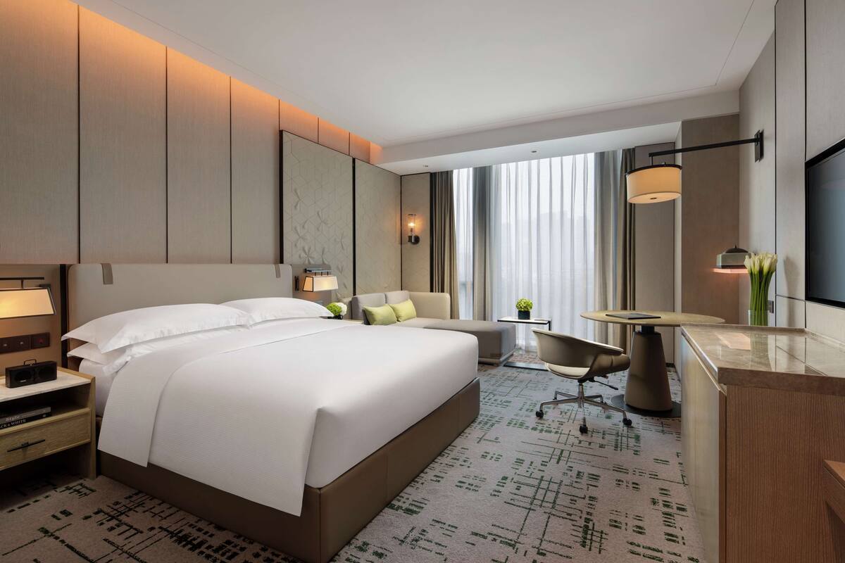 Habitación de hotel moderna con una cama grande, un escritorio, una silla y un televisor.