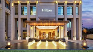 A modern hotel entrance with a large illuminated sign, a covered entrance, and a water feature in front. - Hilton Chengdu Chenghua - Close to Panda Base and Chengdu East Railway Station (Chengdu)