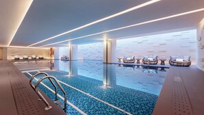 A modern indoor swimming pool with clear blue tiles, lounge chairs, and contemporary lighting. - Hilton Chengdu Chenghua - Close to Panda Base and Chengdu East Railway Station (Chengdu)