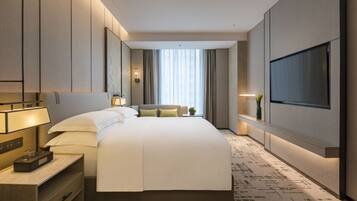 A modern hotel room with a large bed, a flat-screen TV, a bedside table with a lamp, and a small plant.