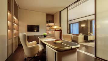 A modern hotel room with a desk, office chair, and a television. There is a sofa and a large window with curtains.