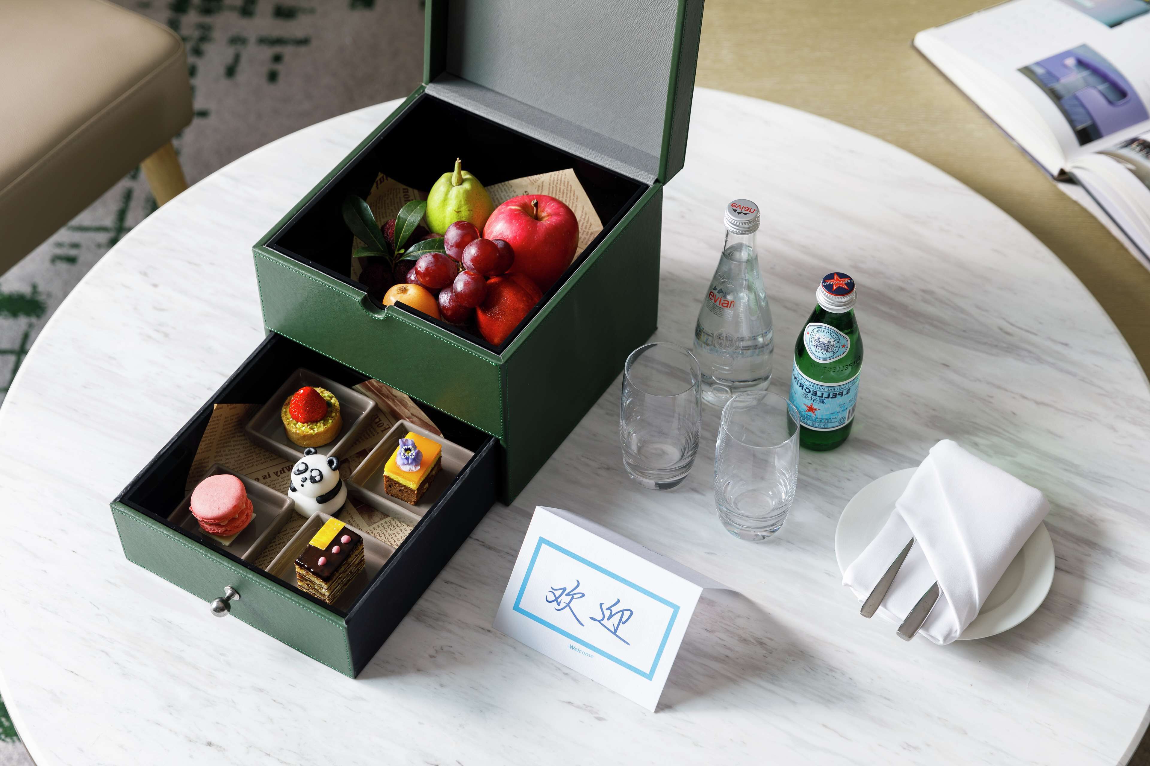 Une boîte verte contenant des fruits, une bouteille et une carte, le tout posé sur une table.
