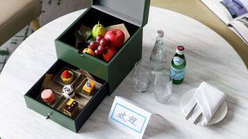 Una caja verde con frutas, una botella y una tarjeta sobre una mesa.
