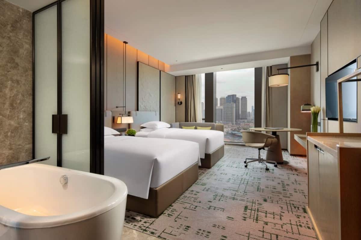 Habitación de hotel moderna con una bañera grande, dos camas, un escritorio y vista a la ciudad.