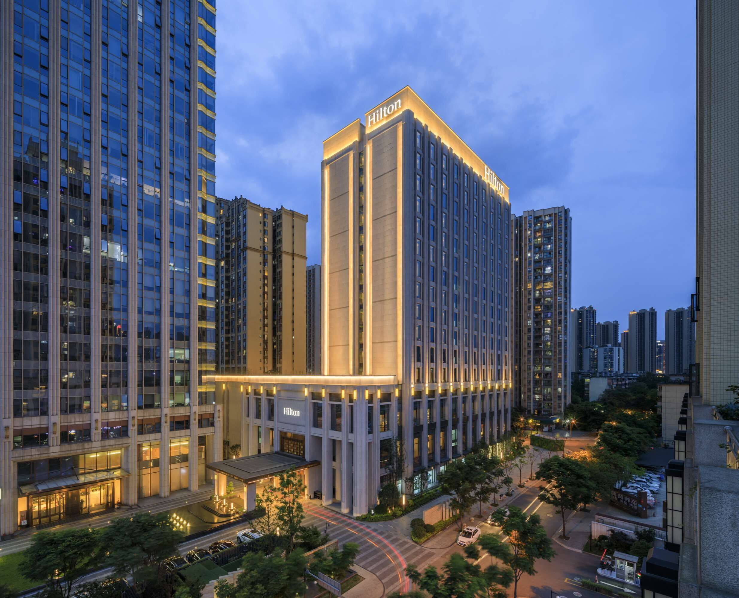 A high-rise hotel with a prominent 'Hilton' sign, surrounded by other tall buildings and a well-maintained urban street.