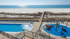 Ein Pool am Strand mit Rutsche, Liegestühlen und Blick auf Strand und Meer.