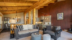 A spacious living room with a wooden ceiling, a sofa, a chair, ottomans, and a kitchen in the background. - Clearview 2 - Amazing Tahoe Views, Dog Friendly, Pool Table, Near Golf (Tahoe City)