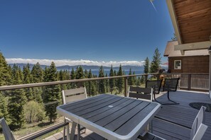 En träveranda med ett bord och stolar, med utsikt över en skog och en sjö, och berg i fjärran.