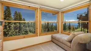 A corner room with large windows, a beige sofa, and a view of a forest and a lake. - Clearview 2 - Amazing Tahoe Views, Dog Friendly, Pool Table, Near Golf (Tahoe City)