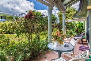 Un espace extérieur aménagé, abrité et doté d’une table et de chaises, entouré d’une végétation luxuriante et offrant une vue sur un bâtiment en arrière-plan.