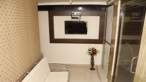 A hotel room with a bed, a TV mounted on the wall, a small table with a vase of flowers, and a glass door leading to a shower area. - Hotel Royal Onix Mumbai (Mumbai)