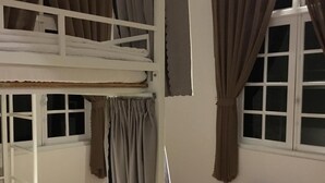 Een kamer met een stapelbed, een raam met gordijnen en een witte muur.
