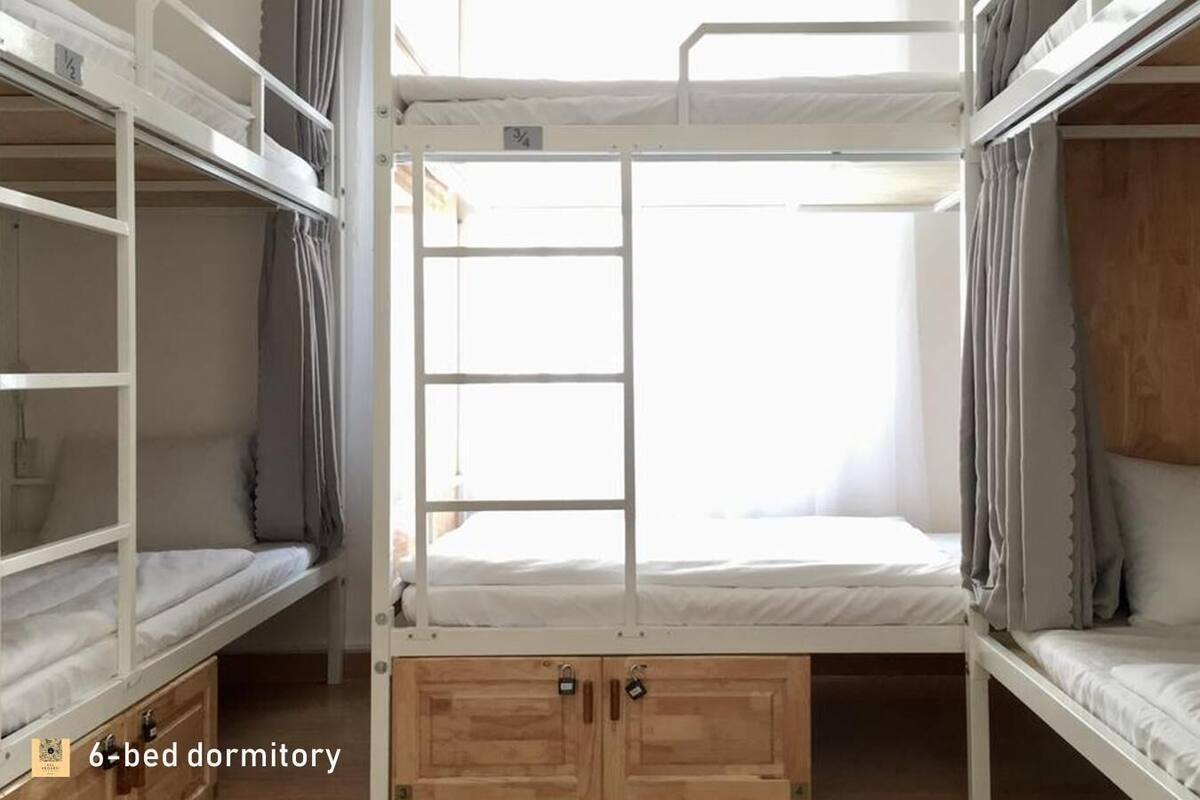 A 6-bed dormitory with bunk beds, wooden cabinets, and a window allowing natural light.