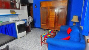 An apartment with a kitchen, a blue sofa, a wooden wardrobe, and a small table with a lamp. - Rositas Hotel (San Juan del Sur)