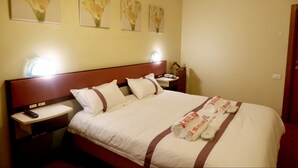 Ein Hotelzimmer mit einem großen Bett, einem Nachttisch mit Telefon und Wandbildern über dem Bett.