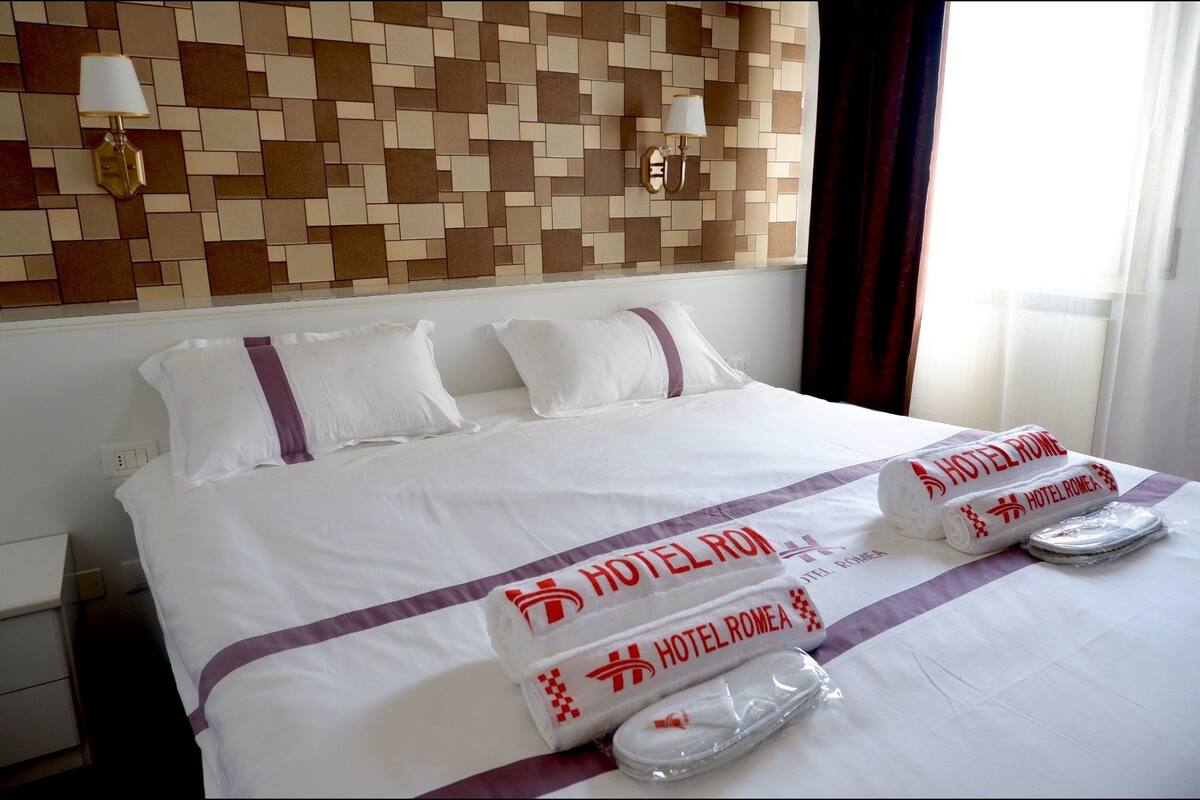 Ein Hotelzimmer mit einem ordentlich bezogenen Bett, einer Wand mit Muster und einem Fenster mit Vorhängen.
