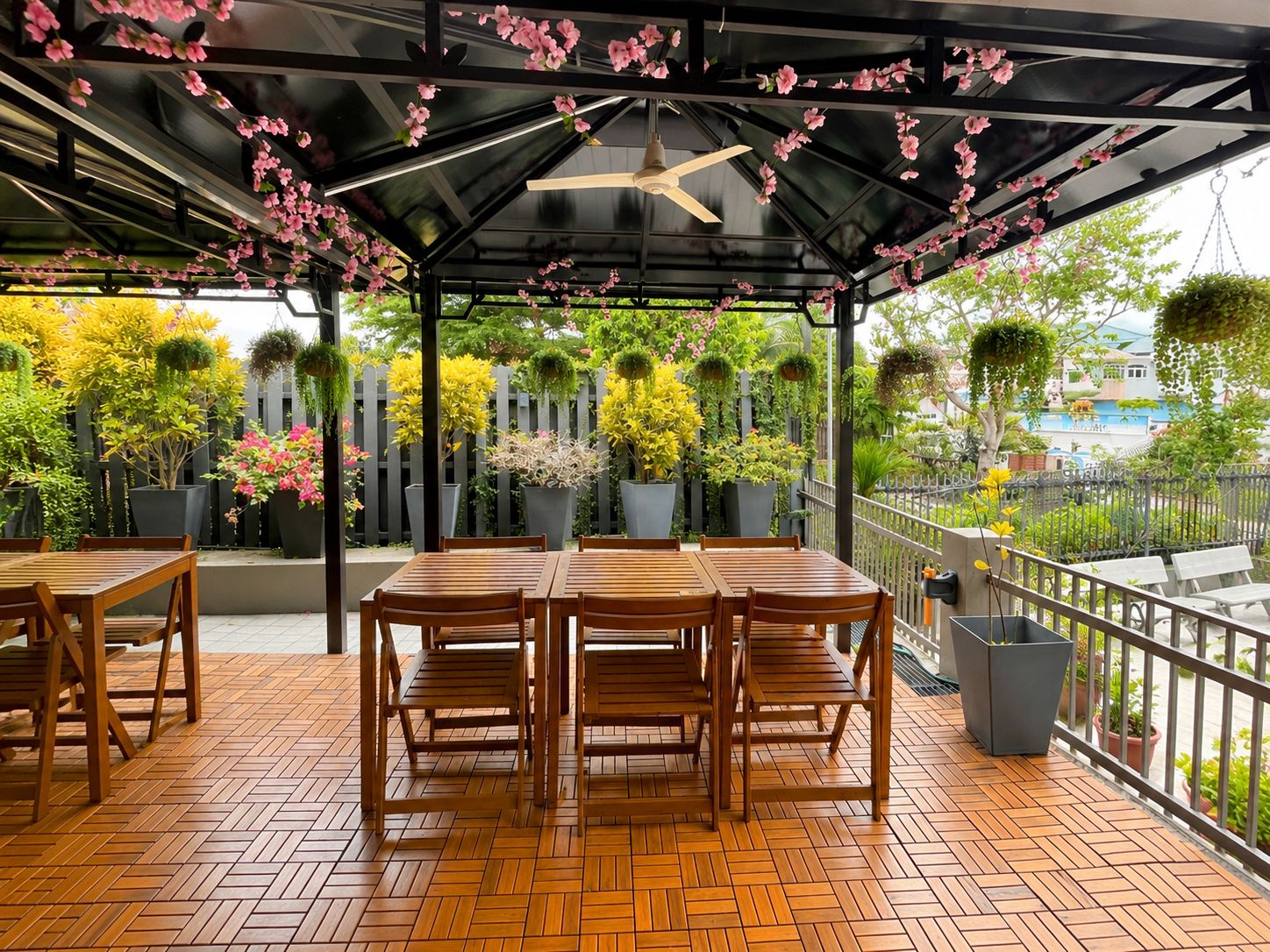 An outdoor patio with wooden tables and chairs, surrounded by potted plants and a wooden fence.