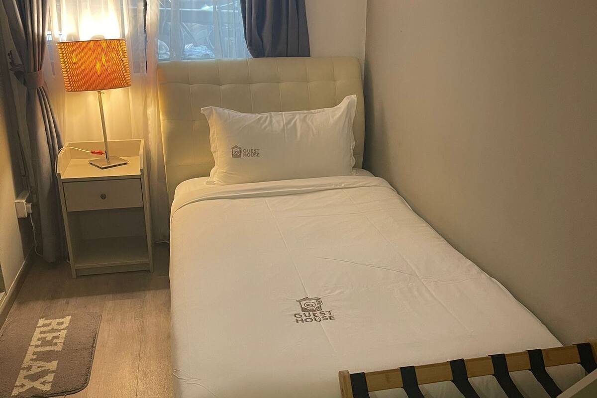 A neatly arranged bedroom with a bed, a bedside table with a lamp, a wooden chair, and a window with curtains.