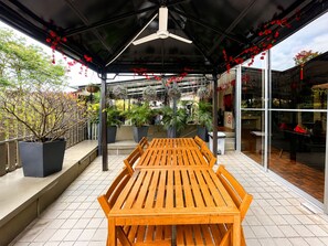 An outdoor patio area with a wooden table and chairs, surrounded by potted plants and a glass enclosure. - K2 Guest House (Singapore)