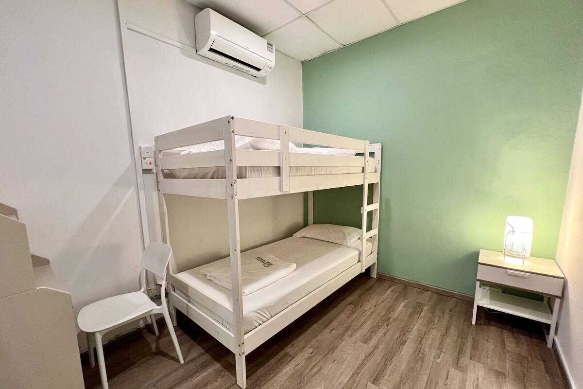 A bunk bed room with a desk and chair, an air conditioner, and a lamp.