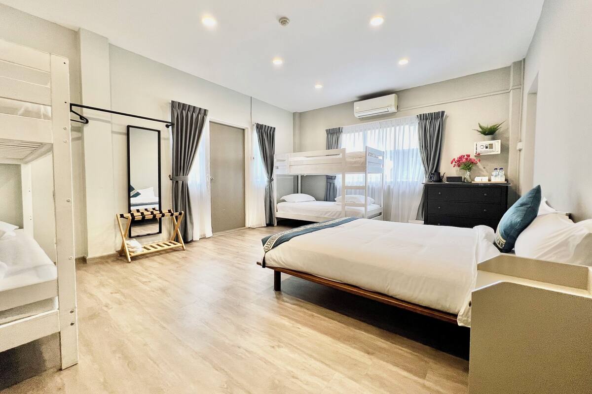 A hotel room with a bunk bed, a desk, a chair, a mirror, and a dresser.