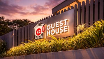 A sign for a guest house with a K2 logo, surrounded by a wooden fence and lush greenery.