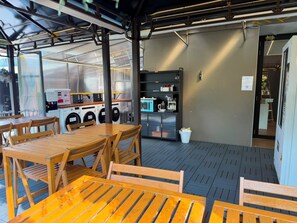 An outdoor seating area with wooden tables and chairs, a washing machine, and a coffee machine. - K2 Guest House (Singapore)