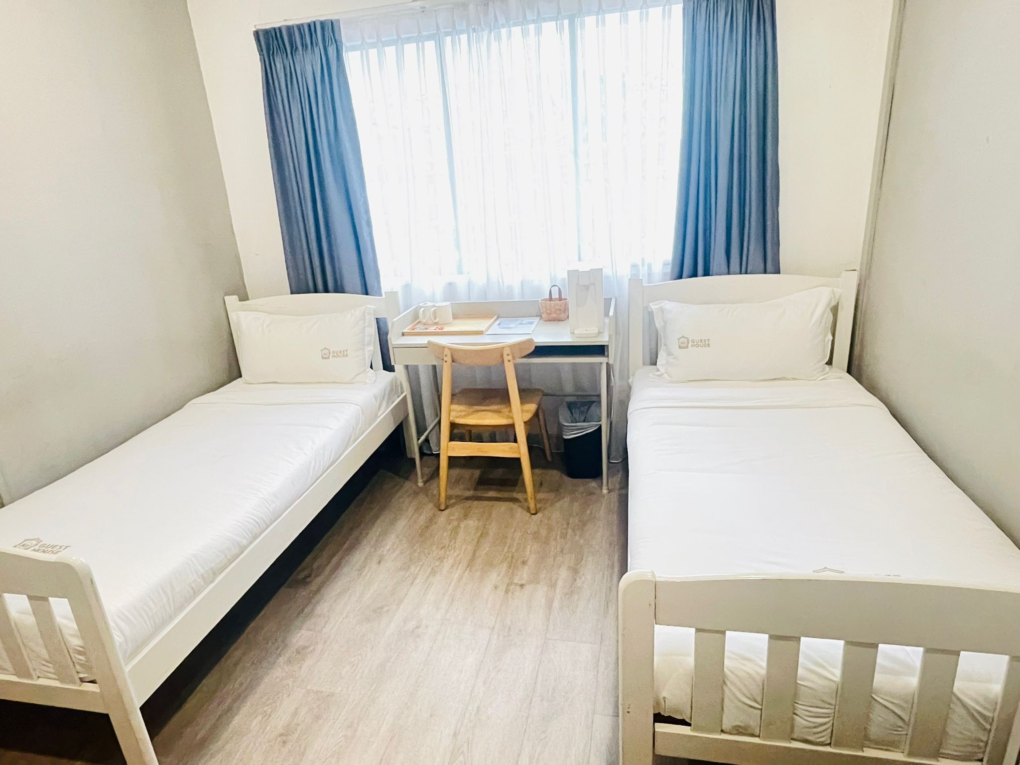 A small, clean room with two single beds, a desk, and a chair.