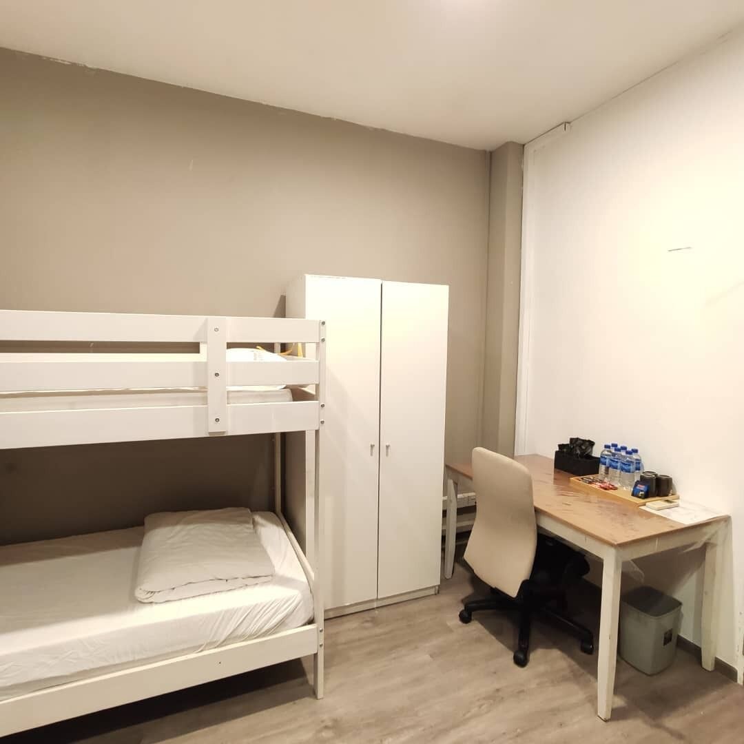 A bunk bed with a desk and chair, a white wardrobe, and a small trash bin.