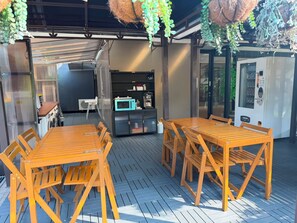 An outdoor seating area with wooden tables and chairs, a washing machine, a microwave, and a vending machine. - K2 Guest House (Singapore)