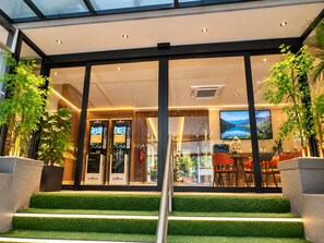 A modern hotel lobby with a glass entrance, indoor plants, and a staircase leading to the upper floor. - K2 Guest House (Singapore)