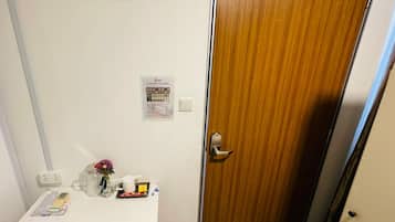 Una habitación con una mesa blanca, una puerta de madera, un interruptor de luz y un aviso en la pared.