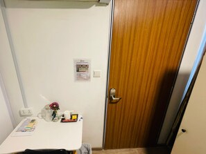 A room with a white table, a wooden door, a light switch, and a notice on the wall. - K2 Guest House (Singapore)