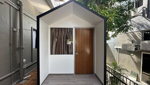 Una habitación moderna y compacta con puerta de madera, ventana con cortinas y un pequeño balcón con barandilla de metal.