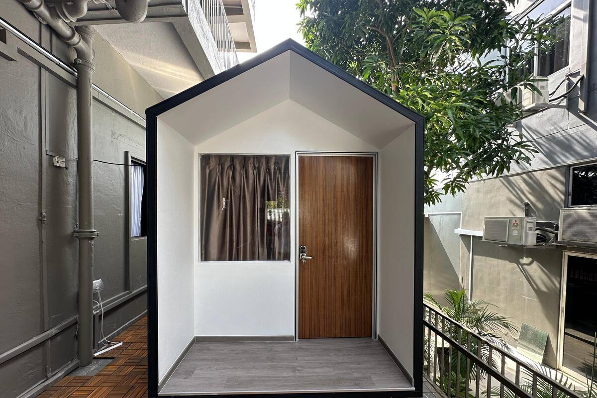 A modern, compact room with a wooden door, a window with curtains, and a small balcony with a metal railing.