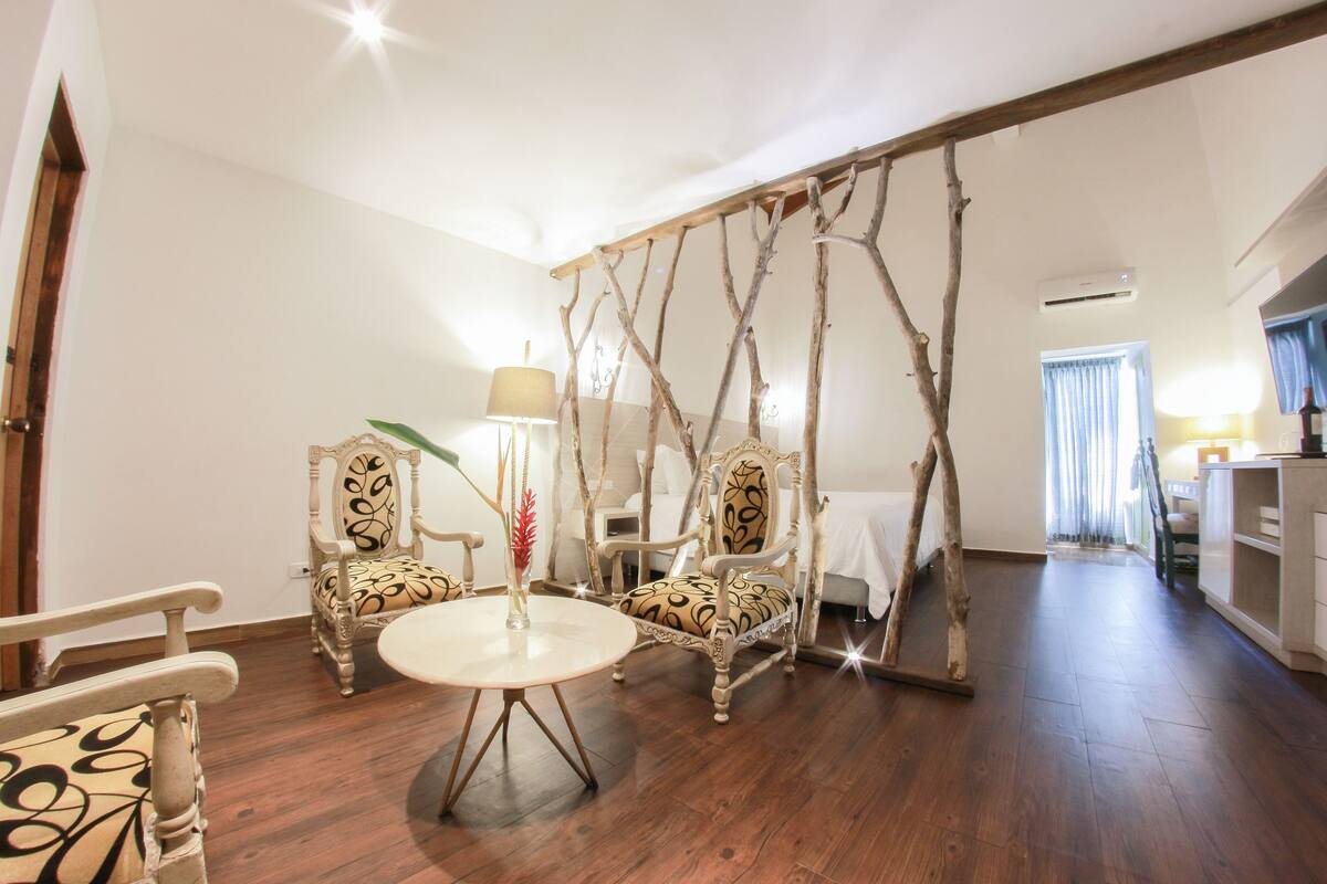 Ein Zimmer mit Holzboden, zwei verzierte Stühle mit gemusterten Polstern, einem runden Tisch und einer dekorativen Holz-Schaukelkonstruktion.