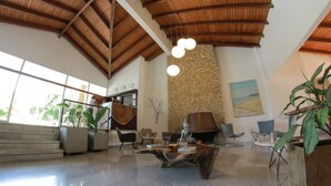 A spacious lobby with a high ceiling, a stone wall, and a Buddha statue. There are several seating areas and a staircase leading to an upper level. - Royal Garden Hotel Boutique (Cali)