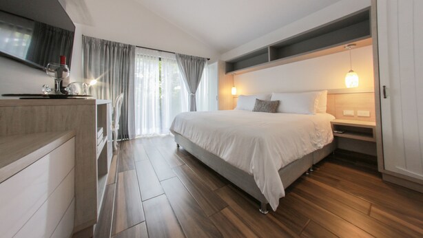A modern bedroom with a large bed, bedside tables, a built-in wardrobe, and a view of the outdoors through a window with curtains. - Royal Garden Hotel Boutique (Cali)