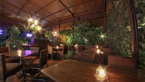 An indoor dining area with wooden tables and chairs, surrounded by lush greenery and plants. - Royal Garden Hotel Boutique (Cali)
