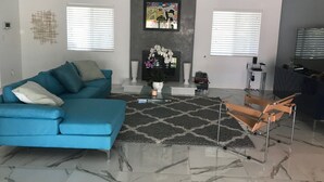 A modern living room with a blue sofa, a glass coffee table, and a fireplace with decorative items. - The Colony House Palm Springs (Palm Springs)