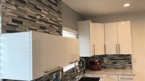 A modern kitchen with white cabinets, a black countertop, and a tiled backsplash. - The Colony House Palm Springs (Palm Springs)