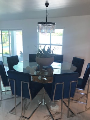 Un comedor moderno con una mesa de vidrio rodeada de sillas tapizadas en azul, una planta en maceta en el centro y una lámpara de araña de cristal colgante.