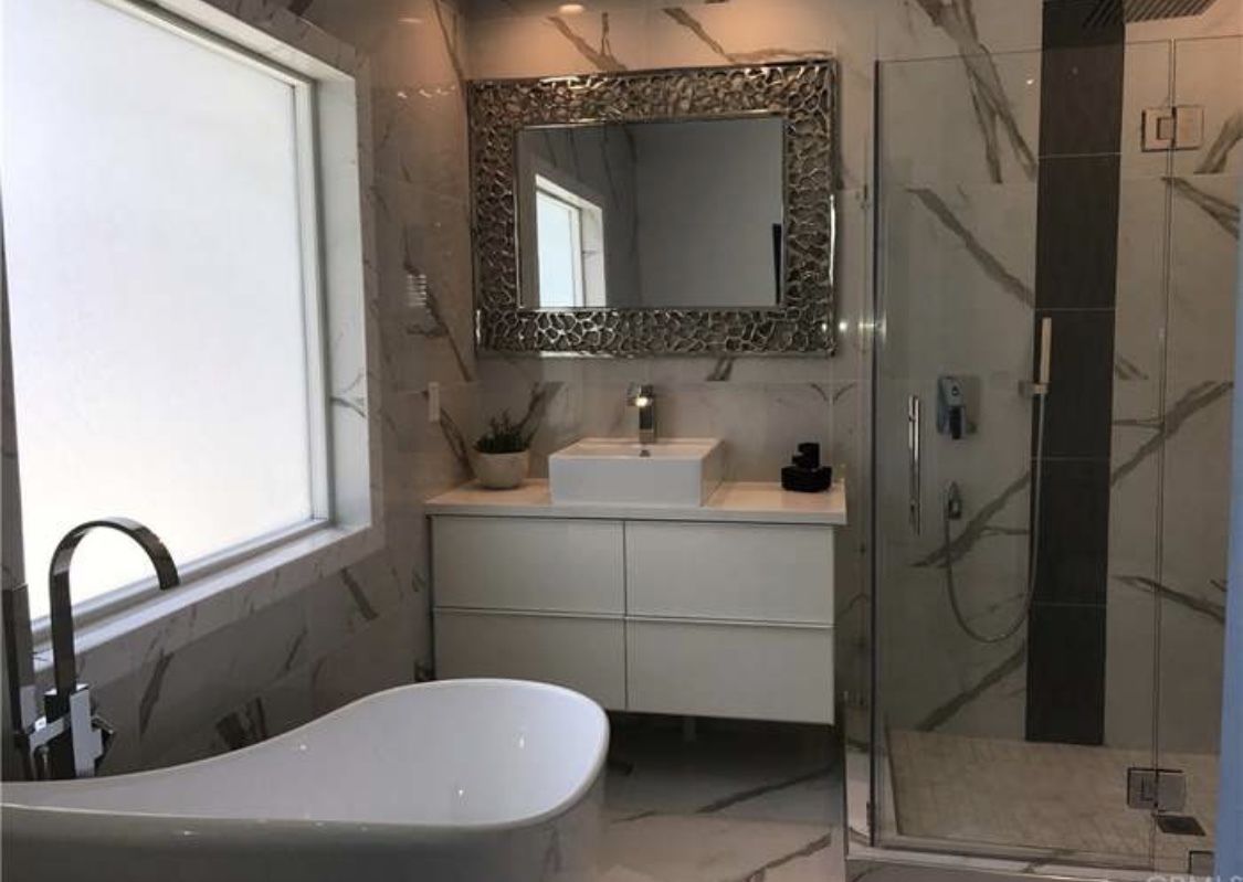 Un baño moderno con una bañera independiente, un espejo grande con marco decorativo y una cabina de ducha.