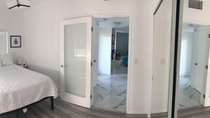 A bedroom with a bed, a nightstand, a potted plant, and a door leading to a bathroom. - The Colony House Palm Springs (Palm Springs)