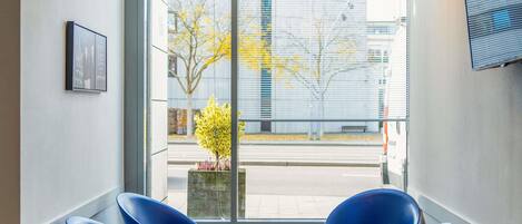 A modern interior with a large window, two blue chairs, a small table, and hanging spherical light fixtures.