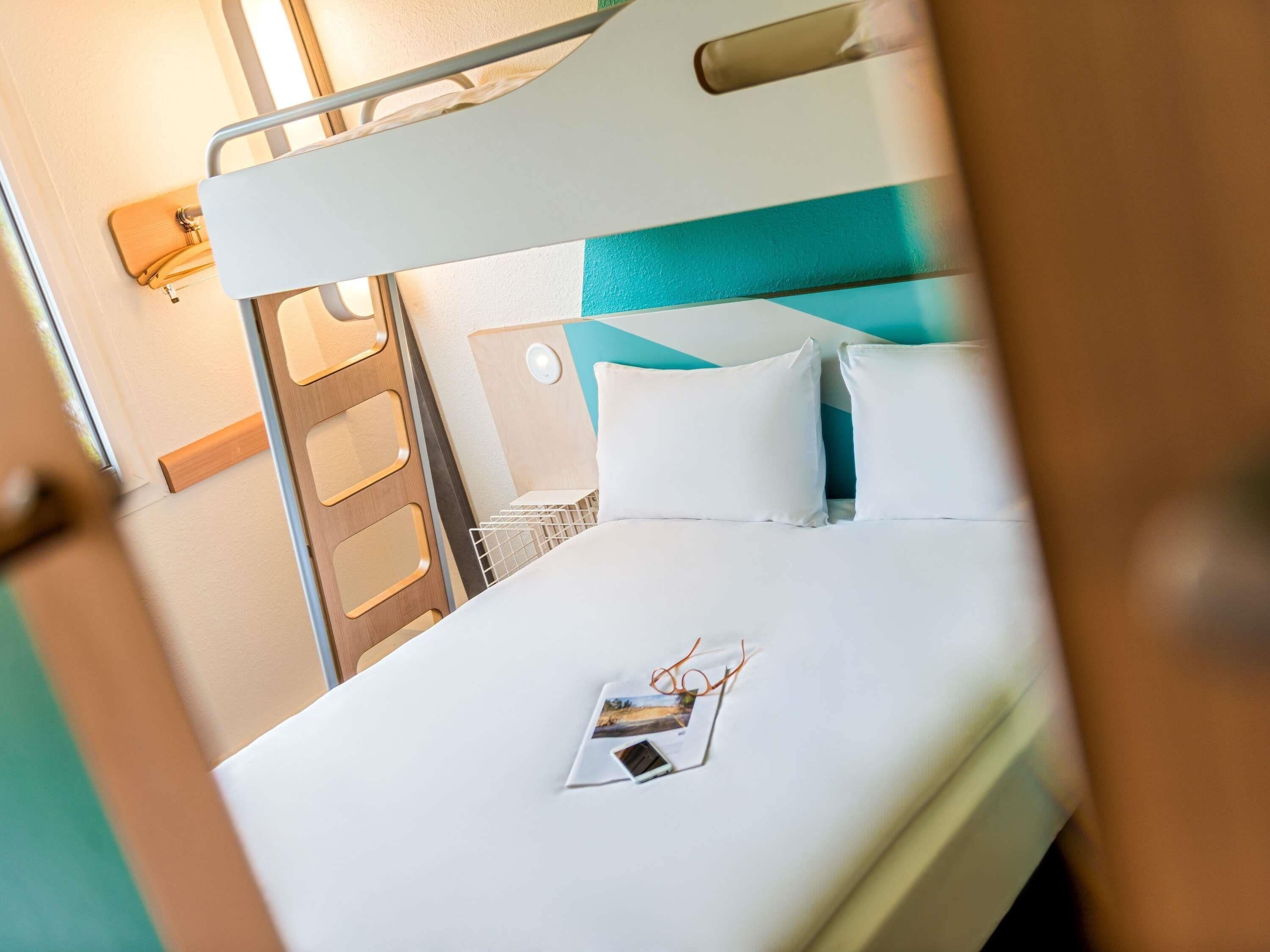 A bunk bed with a white mattress, a teal headboard, and a white pillow.